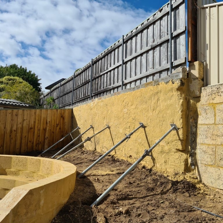Exposed stabilised sandy ground beneath a boundary fence, with temporary props